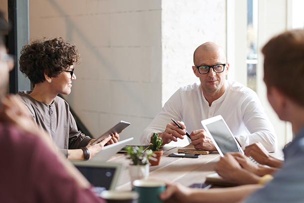 Some professional people sitting around a table having a meeting, wearing smart but casual clothing. They are holding digital tablets and in discussion 